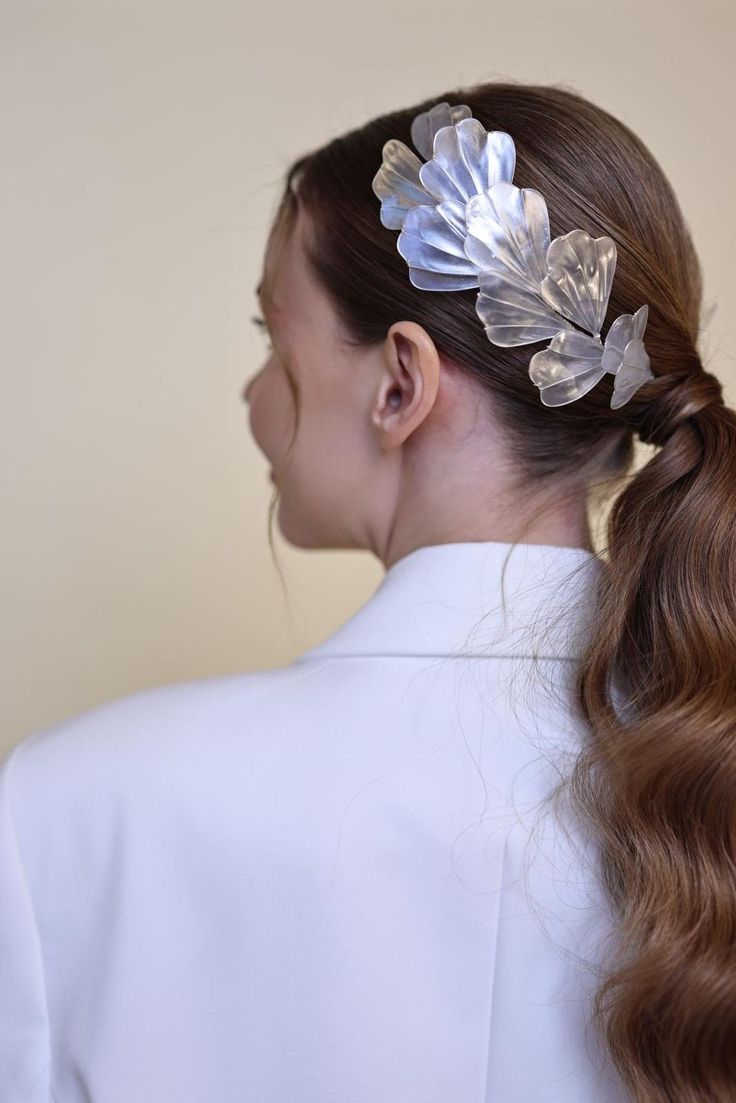 a woman with long hair in a ponytail wearing a white blazer and flower clip