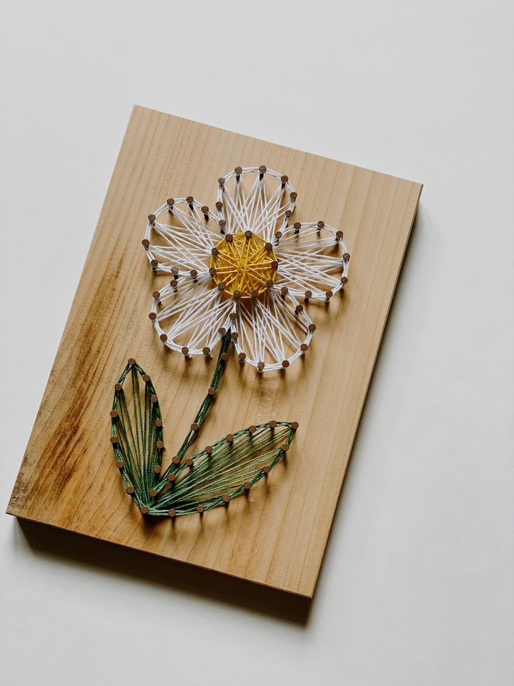 a flower made out of string sitting on top of a wooden board