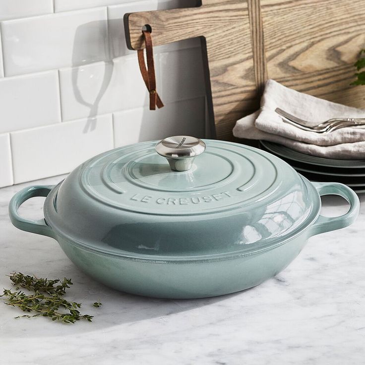 a blue casserole sitting on top of a counter next to plates and utensils