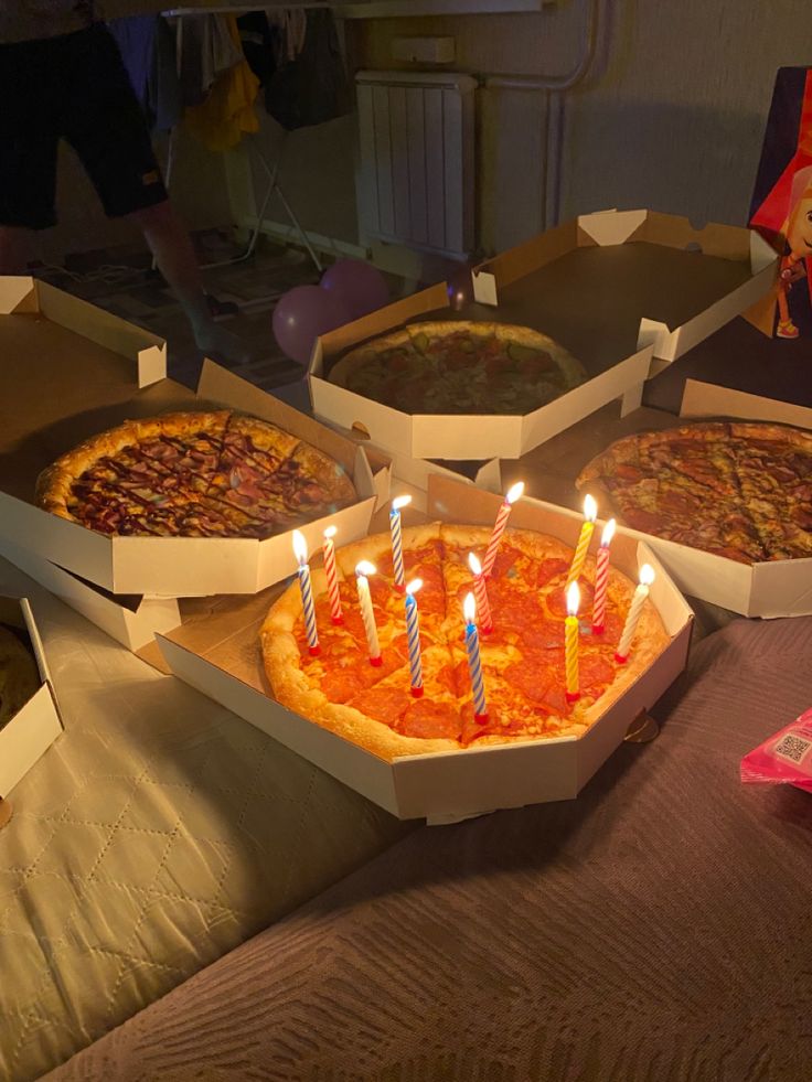 three pizzas with candles are sitting in boxes on a table next to each other