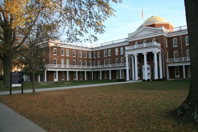 an old brick building with columns and arches on the front is surrounded by grass and trees