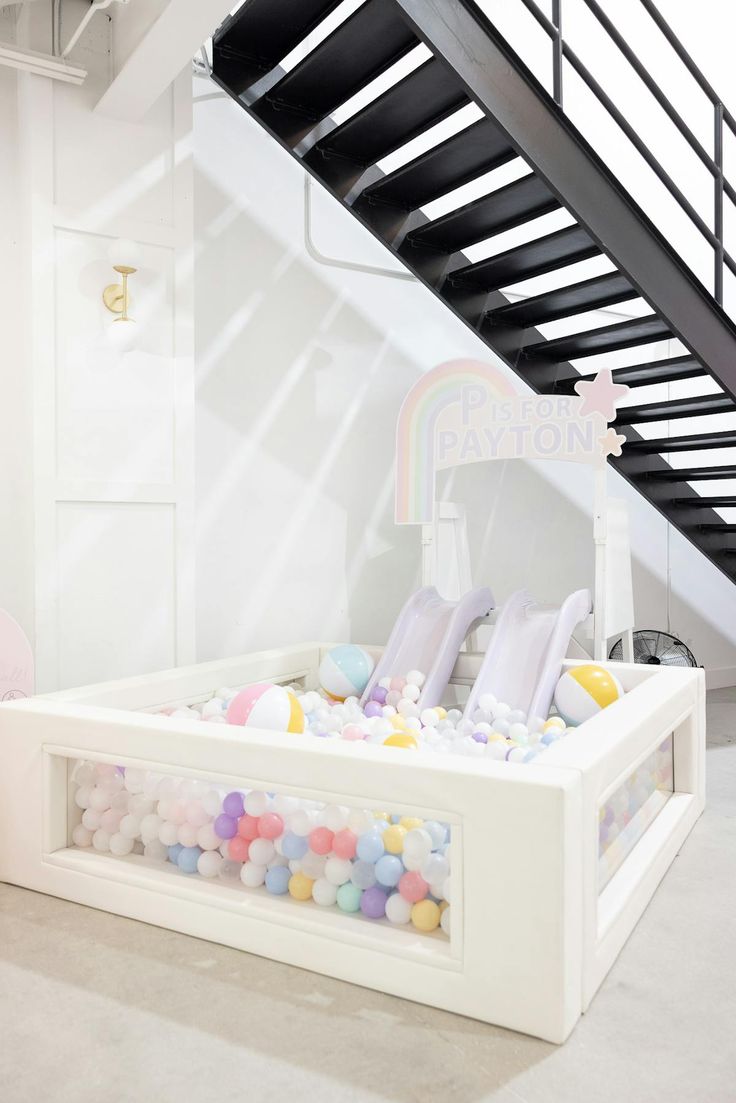 a white bed with lots of colorful balls on the bottom and underneath it, under a stair case