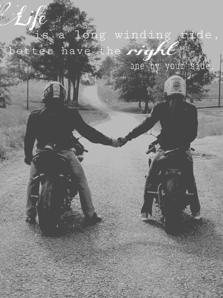 two people riding motorcycles holding hands on a dirt road