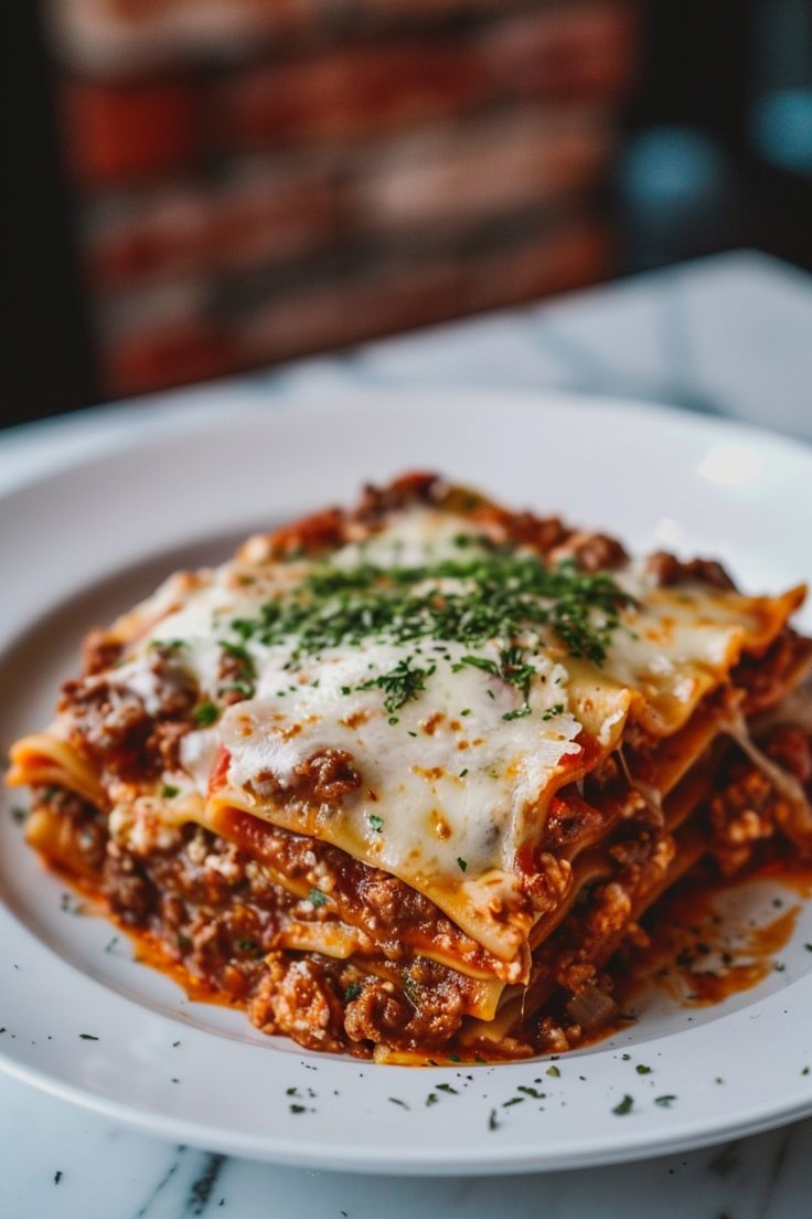 a white plate topped with lasagna covered in cheese and sauce on top of a marble table