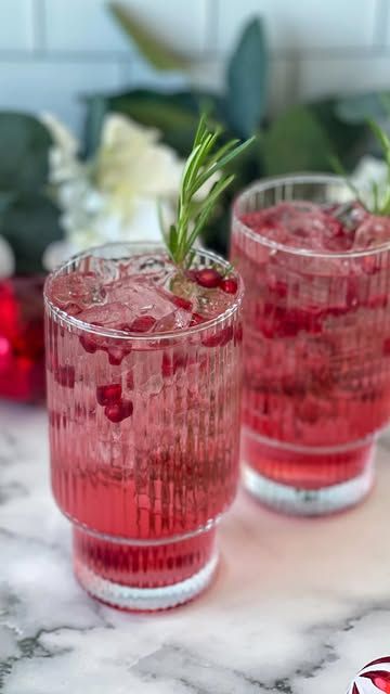 two glasses filled with red liquid and garnished with rosemary on the rims