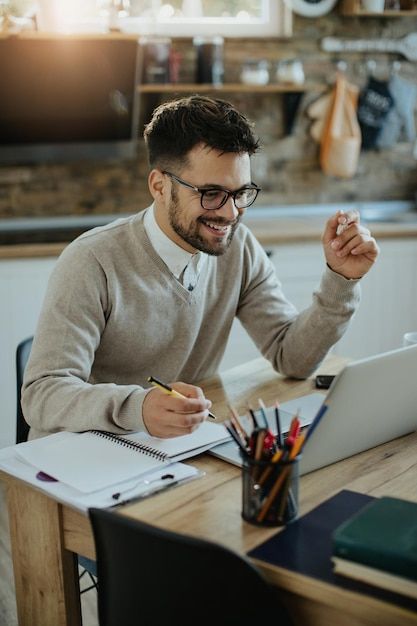 a man sitting at a table with a laptop and pen in his hand, smiling