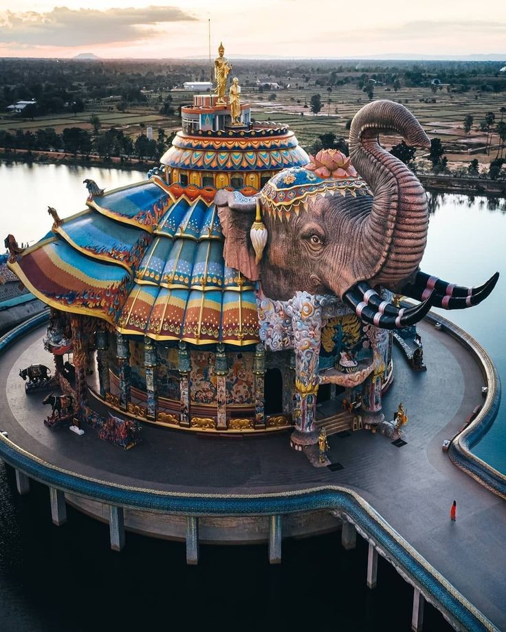 an elephant statue sitting on top of a building next to a body of water at sunset