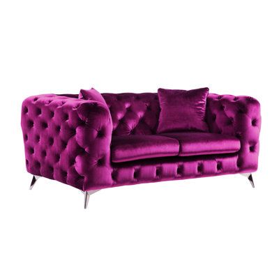 a purple velvet couch with two pillows on it's back and one arm facing the camera