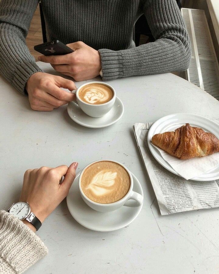 two people sitting at a table with coffee and croissants