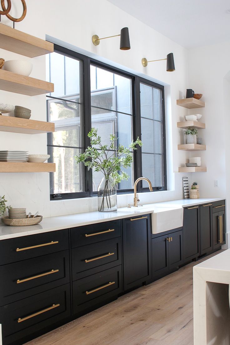 a kitchen with black cabinets and white counter tops, gold pulls on the doors and shelves