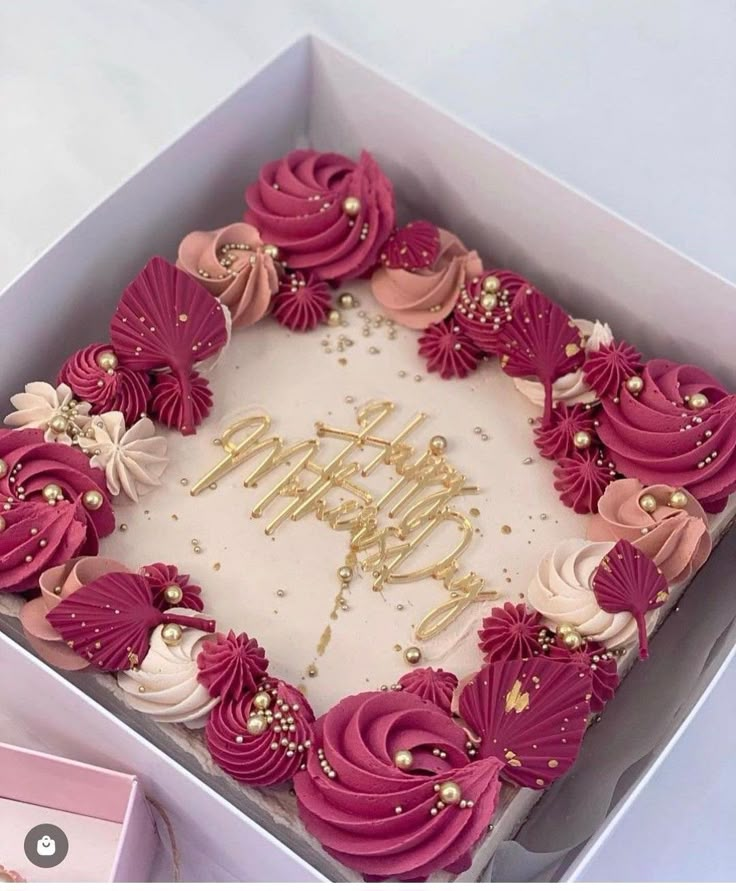 a birthday cake in a box with pink frosting and gold decorations on it's side