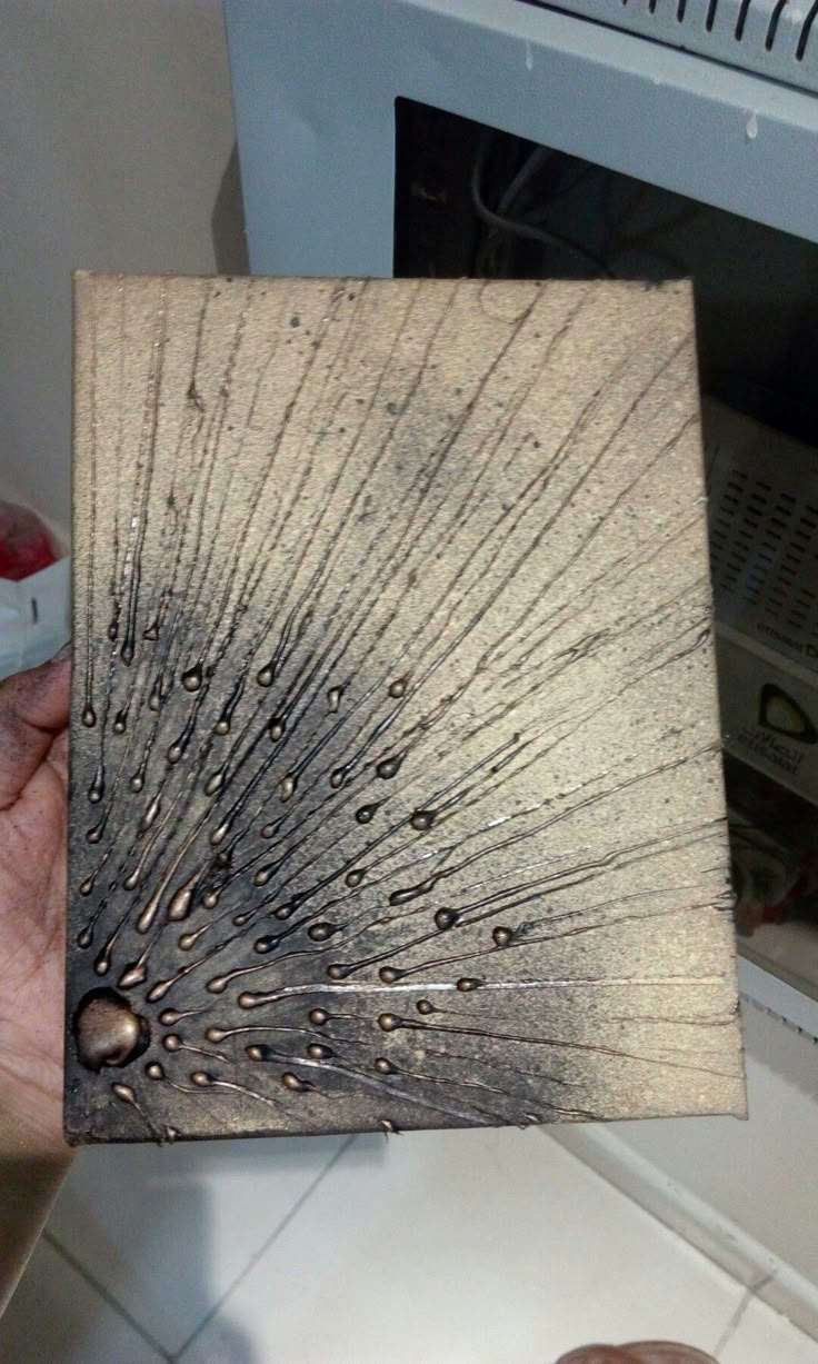 a person holding up a piece of wood with water drops on it and a microwave in the background