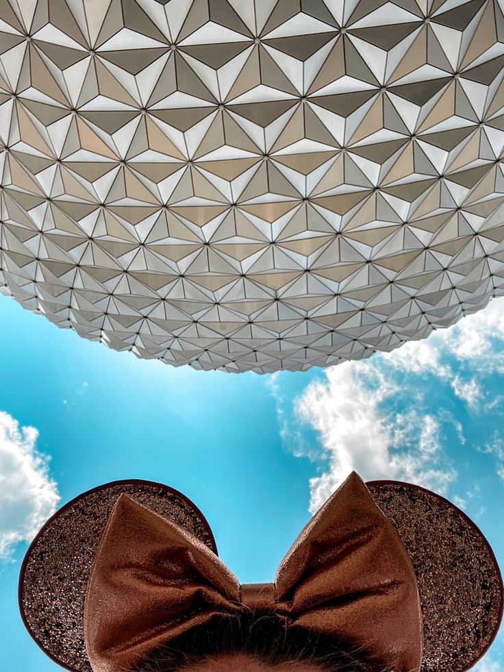 a person wearing a hat and bow tie under a blue sky with clouds in the background