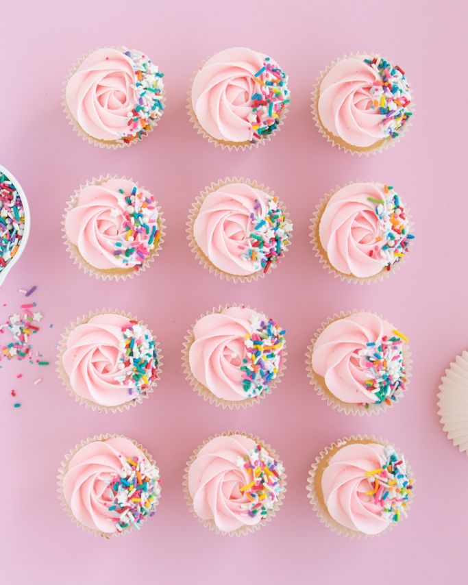 cupcakes with pink frosting and sprinkles on a pink background