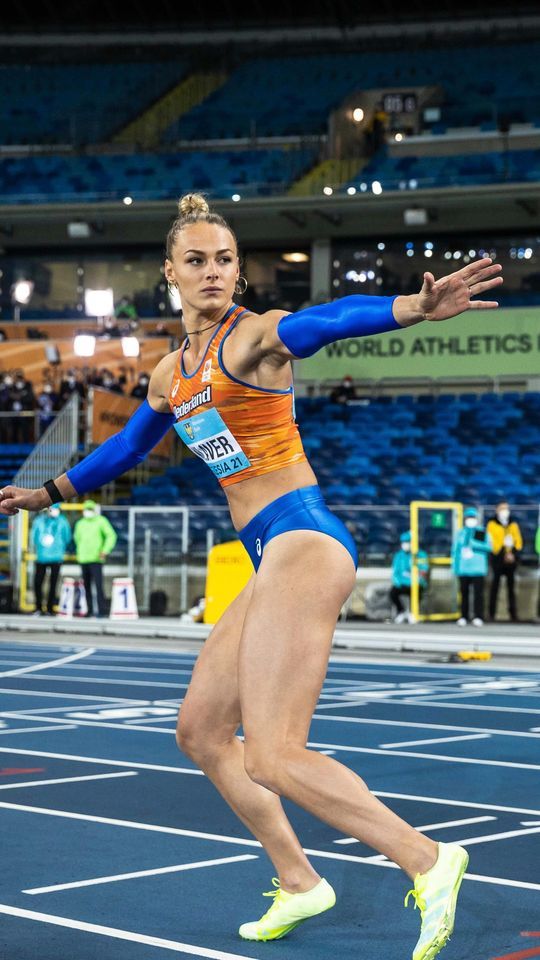 a female athlete in an orange and blue outfit is running on a track with her arms outstretched