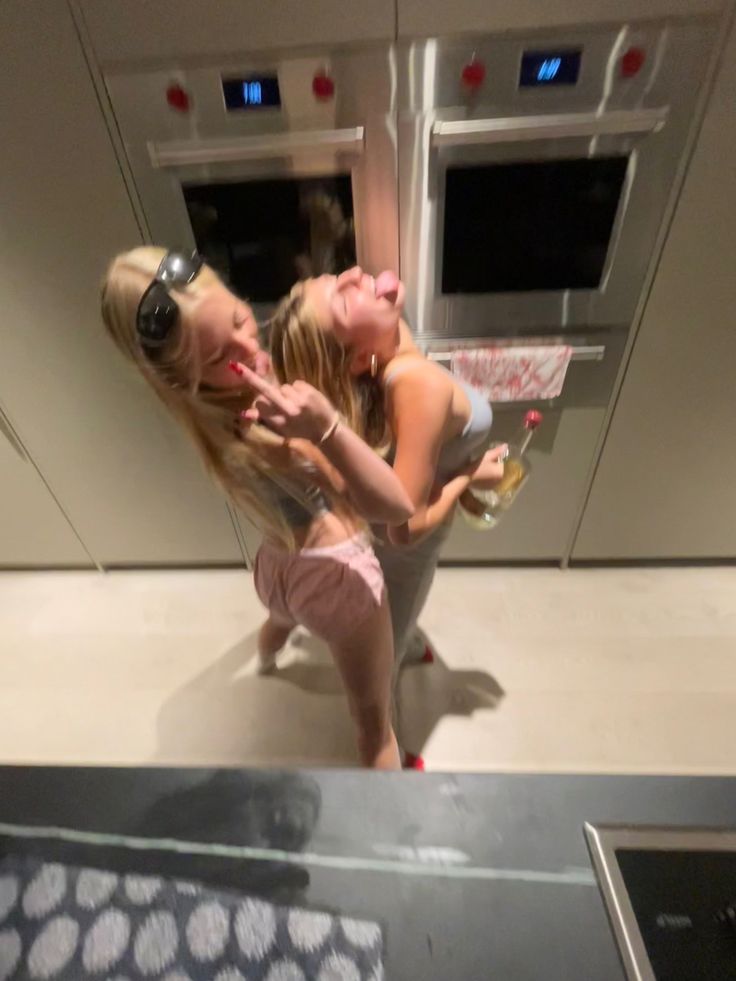 two young women are dancing in the kitchen