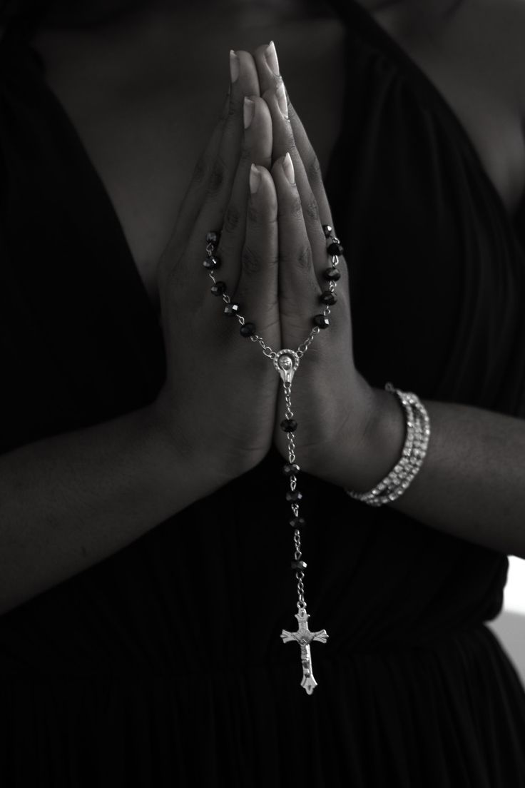 a woman in a black dress is holding her hands together with a cross on it