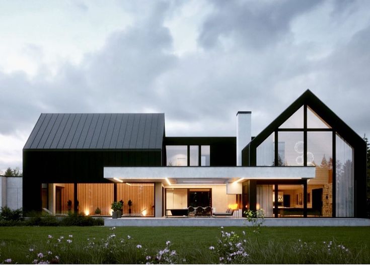 a modern house with large windows and lots of grass in the front yard at dusk