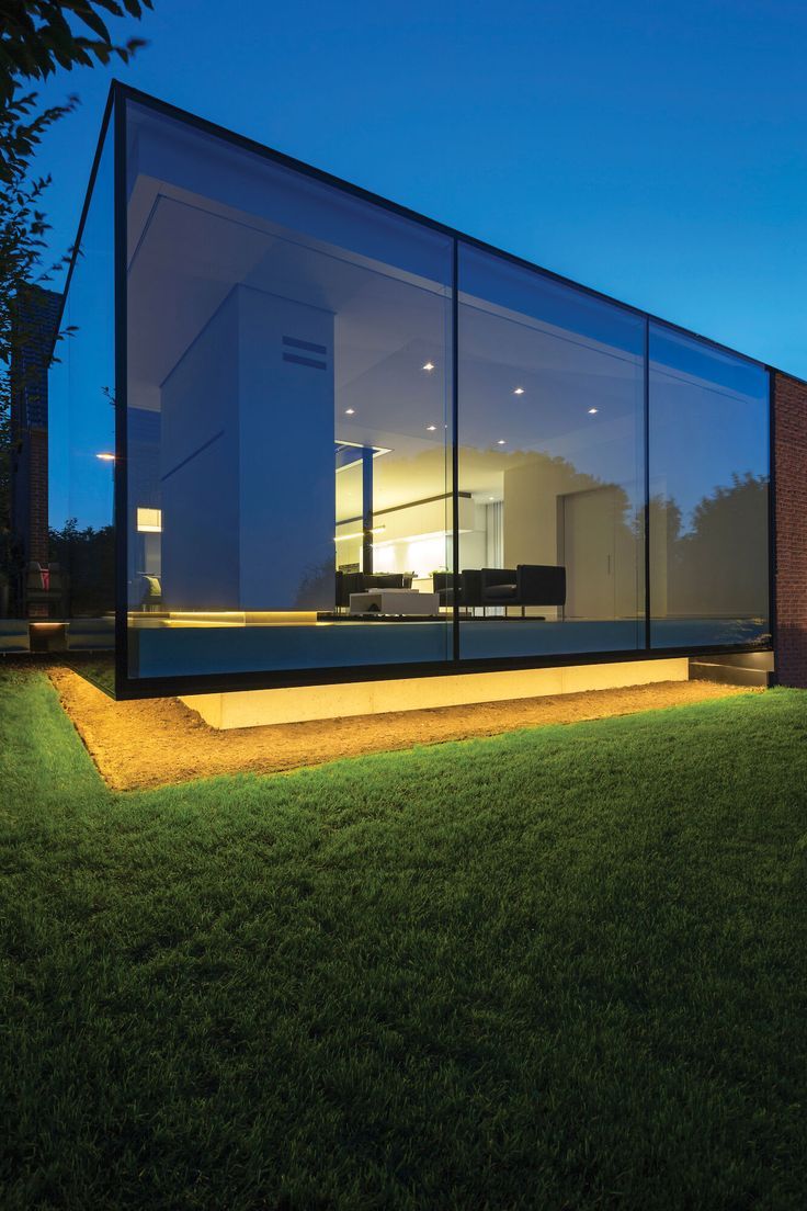 a modern glass house in the middle of a grassy area at night with lights on