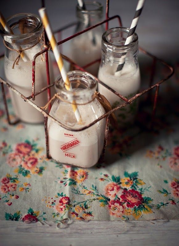 three jars with straws in them are sitting on a floral tablecloth and one is filled with milk