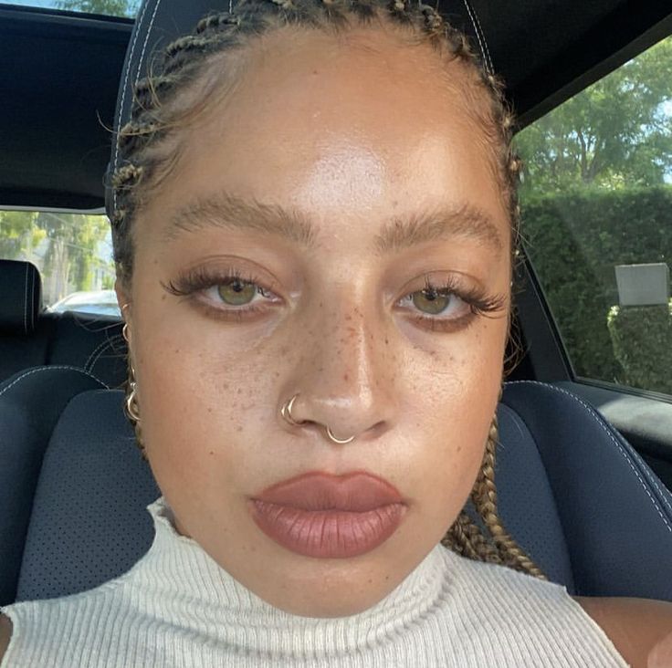 a woman with braids and nose piercing in the back seat of a car looking at the camera