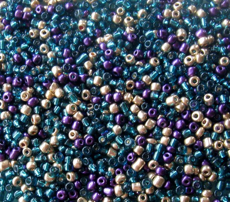 purple and green beads are arranged together on a blue tablecloth with gold trimmings