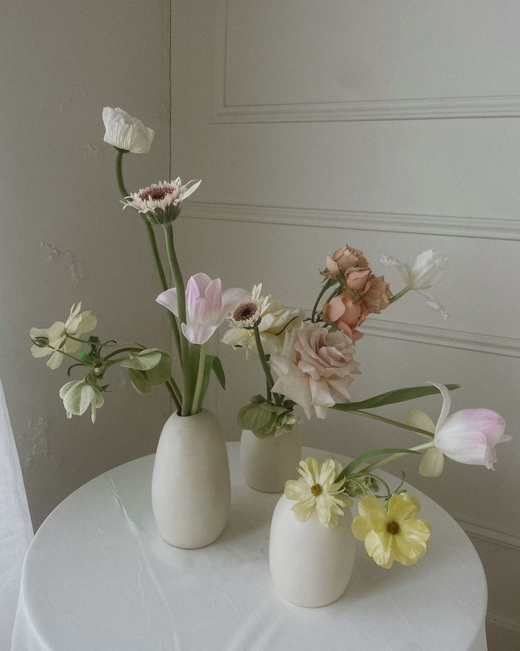 three white vases with flowers in them on a table