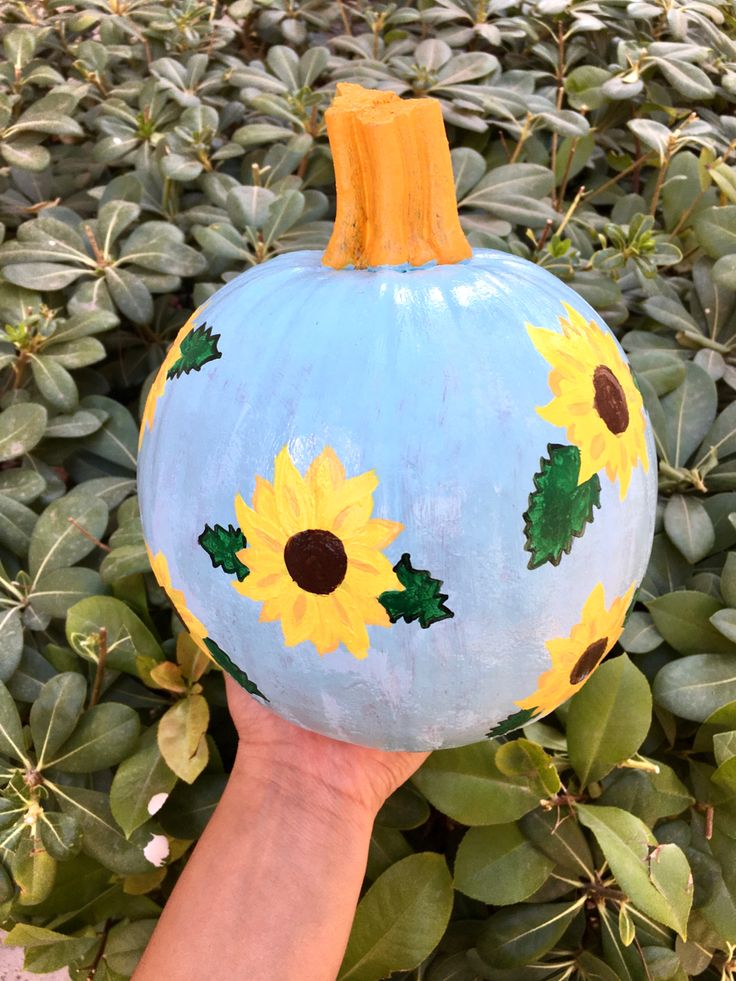 a painted pumpkin with sunflowers on it is held by a person's hand