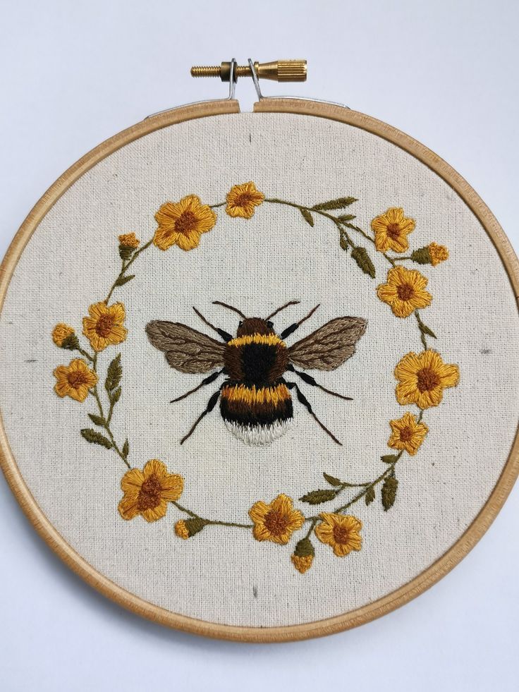 a cross stitch bee with yellow flowers in the center on a white background is framed by a wooden hoop