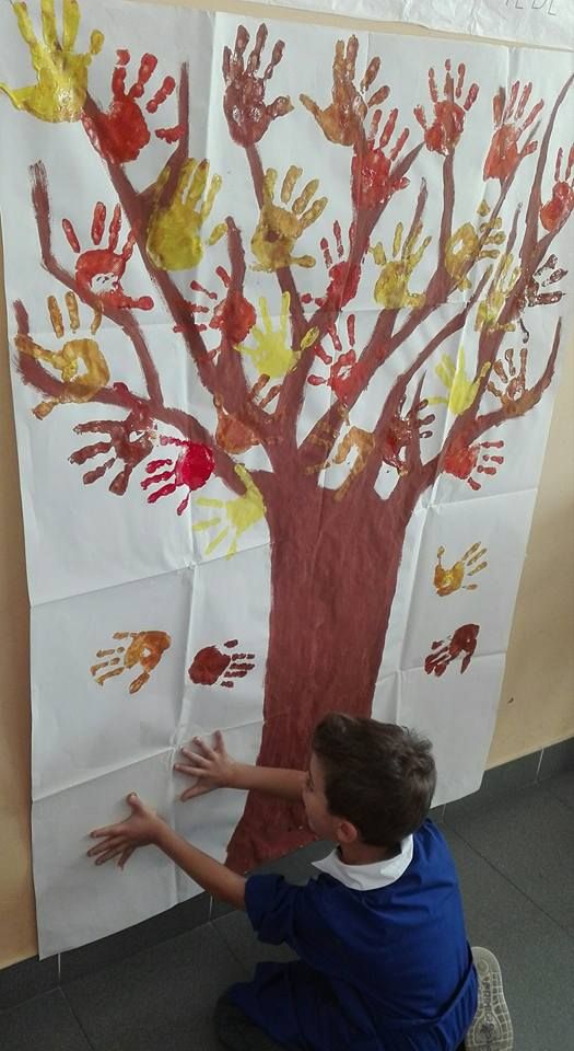 a young boy sitting on the floor in front of a tree made out of handprints