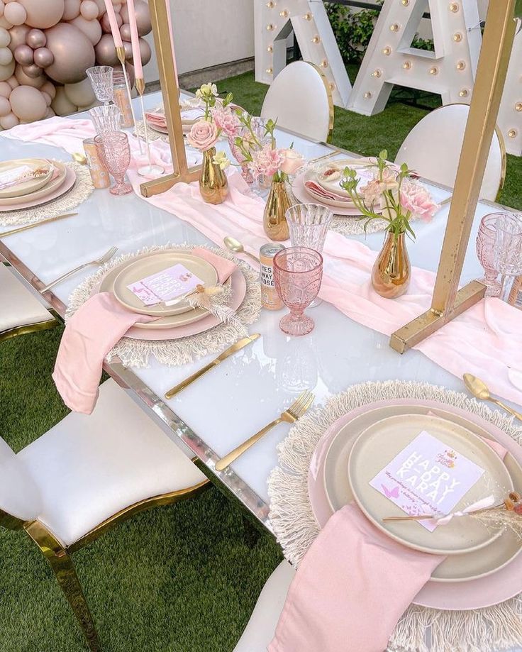 the table is set with pink and gold plates, napkins, and place settings