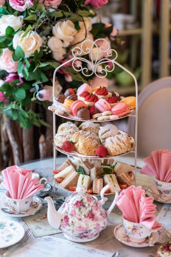 an assortment of pastries and teacups on a table with flowers in the background