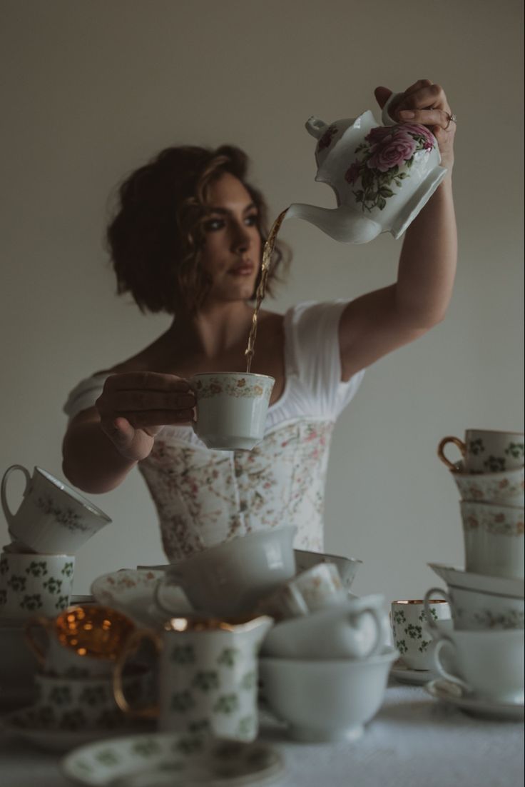 a woman pouring tea into a cup on top of a table with cups and saucers