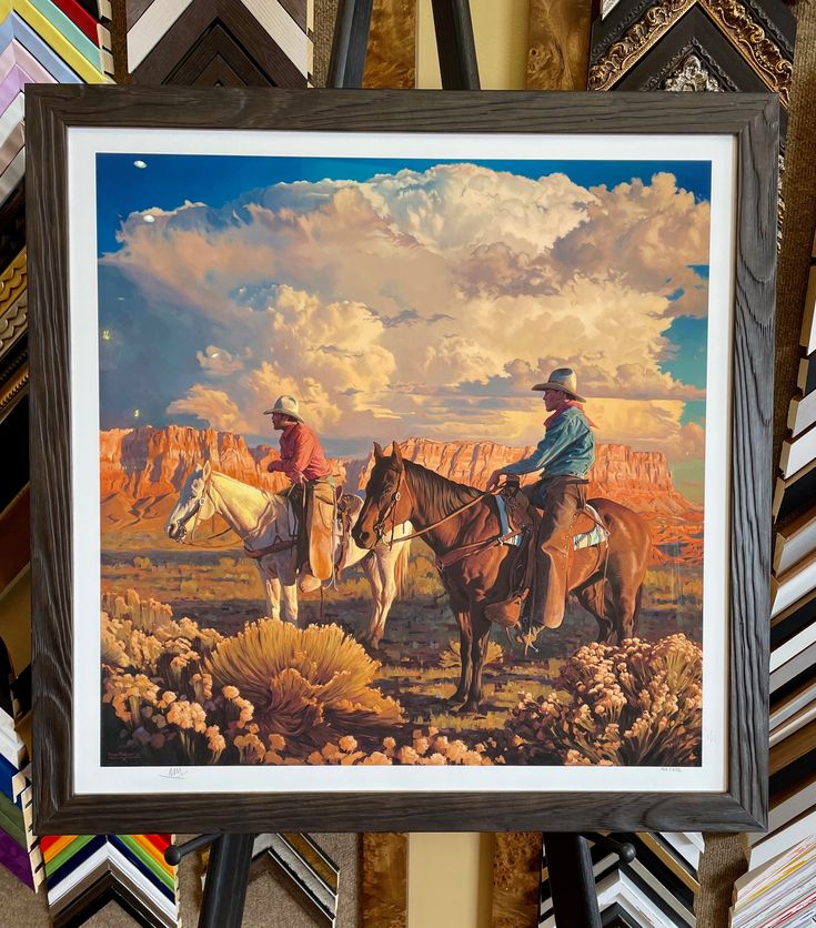 two cowboys on horseback in the desert with cactus and mountains behind them, framed art print