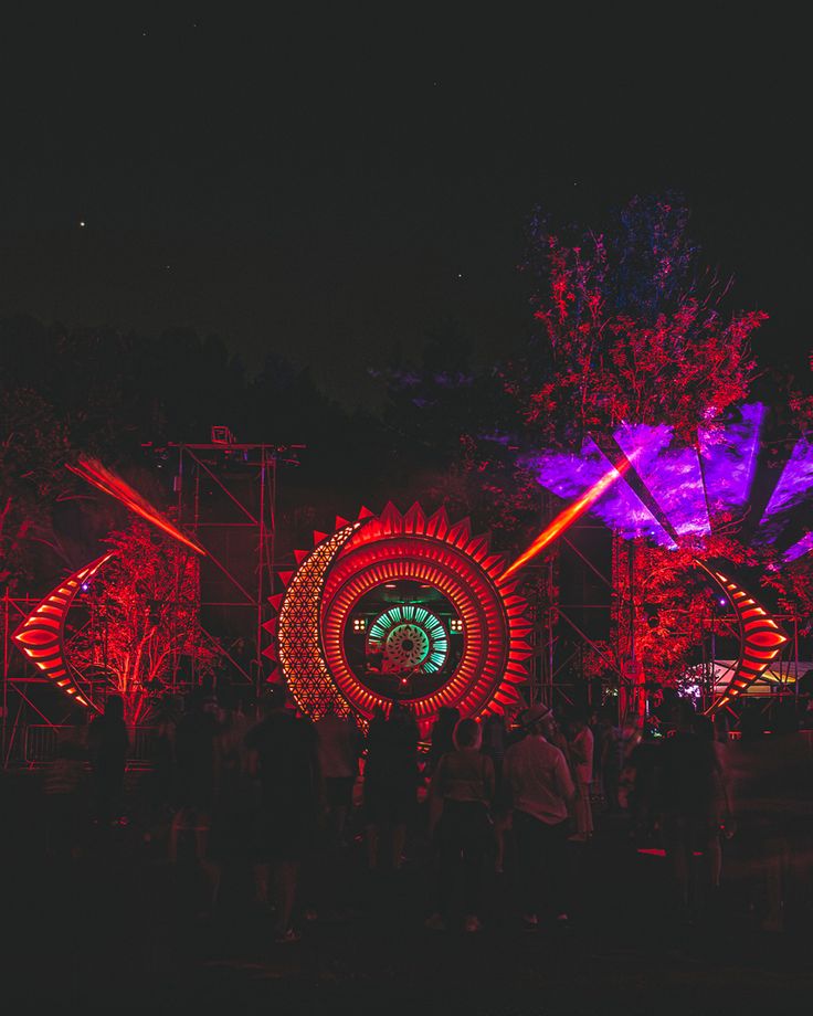 people are standing around in front of an illuminated display at night with red and purple lights