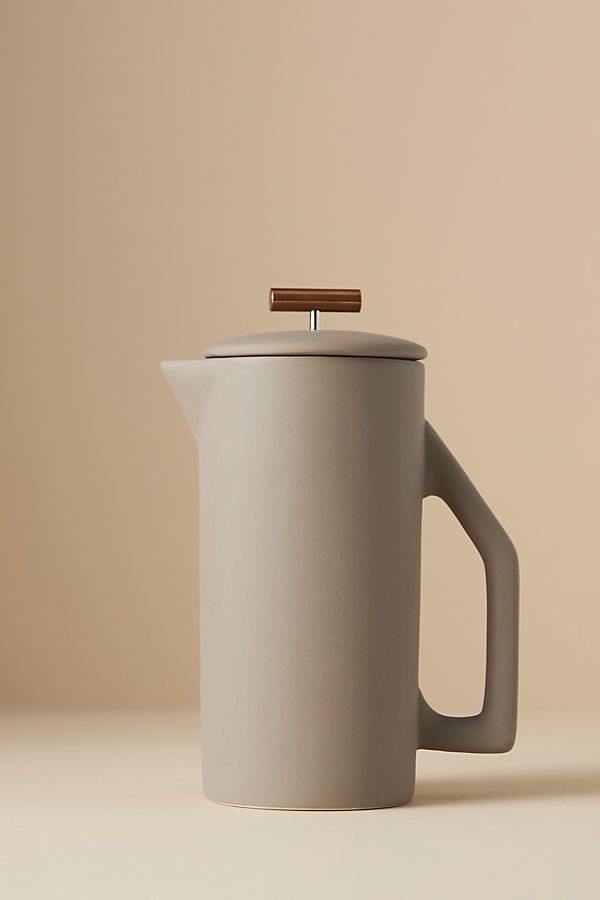 a white coffee pot with a wooden handle on a beige table top, next to a brown wall