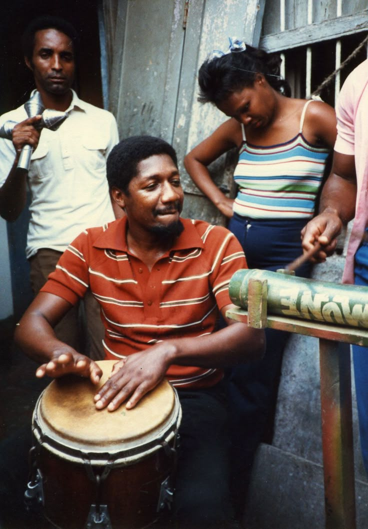 a group of people standing around a man sitting on top of a drum