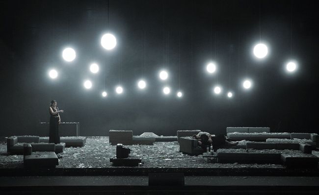 two people standing on stage in the dark with bright lights above them and benches below