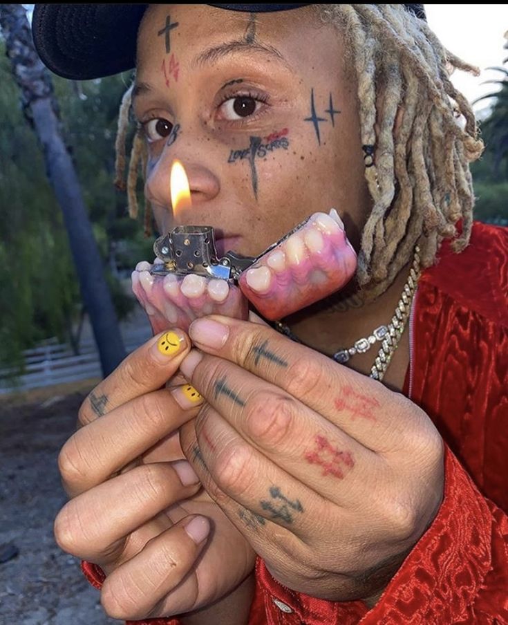 a man with dreadlocks holding a lighter in his hand and wearing tattoos on his face