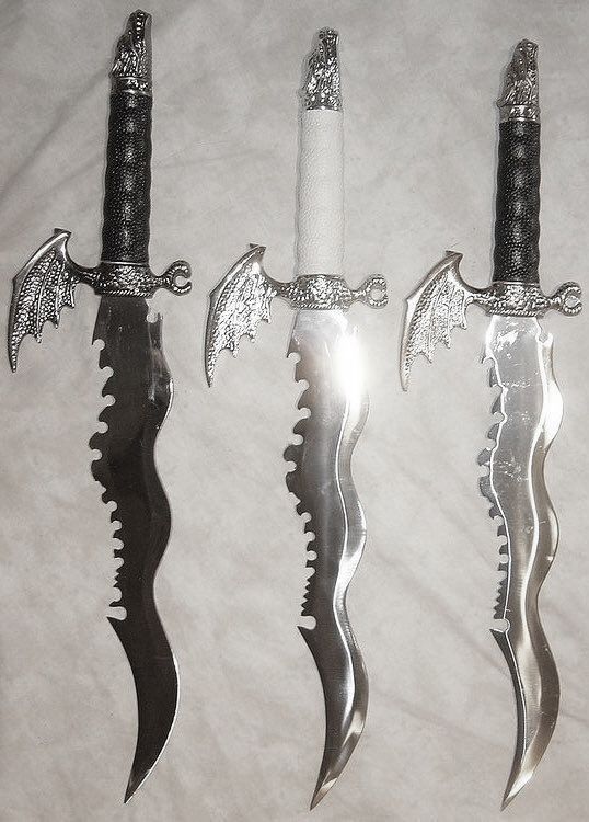 three knives with dragon handles are on a white sheet and one knife has two black blades