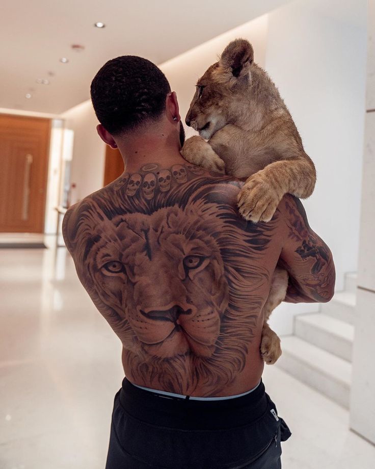 a man with a lion tattoo on his back is holding a baby lion up to his chest