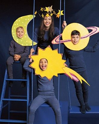 three children are posing on stage with paper stars and moon cutouts in front of them