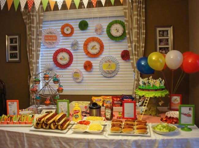 a table topped with lots of food next to a window covered in balloons and streamers