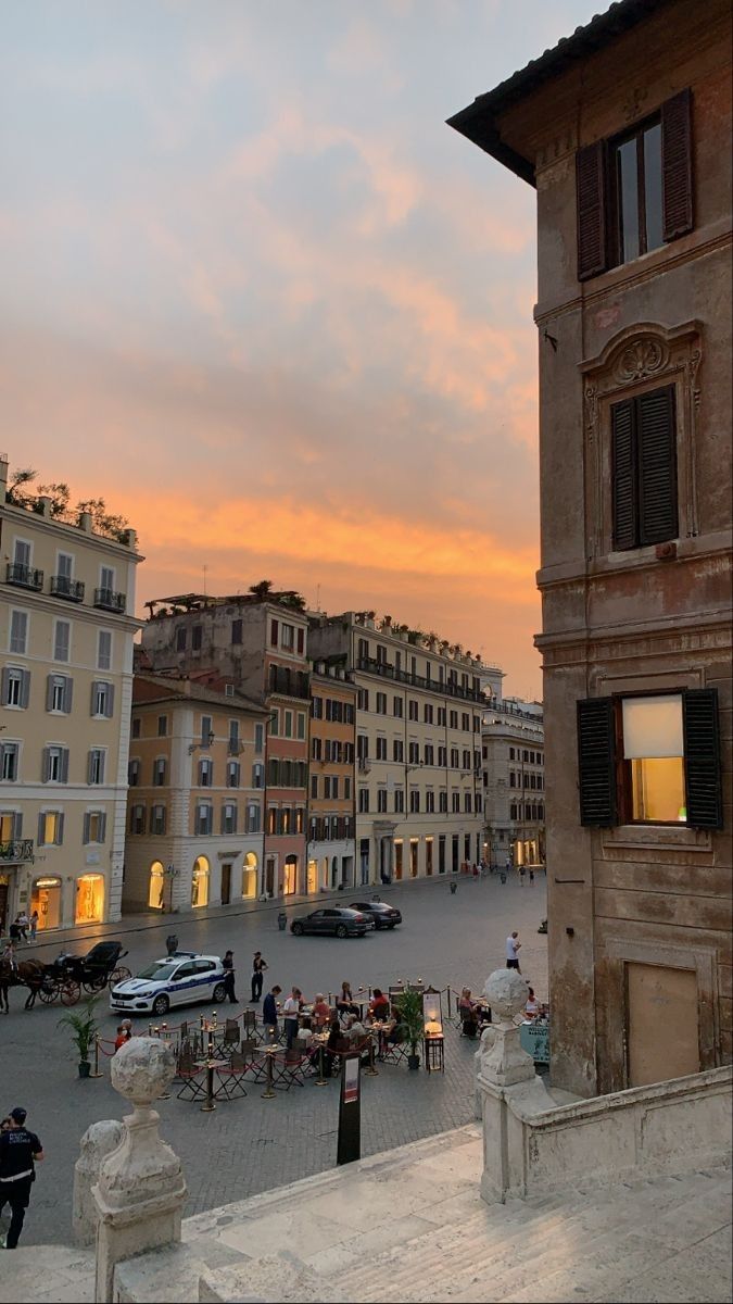 the sun is setting over an old town square with many buildings and people walking around