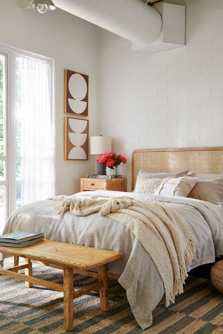 a bed sitting in a bedroom next to a window with white curtains and blankets on top of it