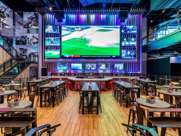 the inside of a sports bar with tables, chairs and televisions on the wall