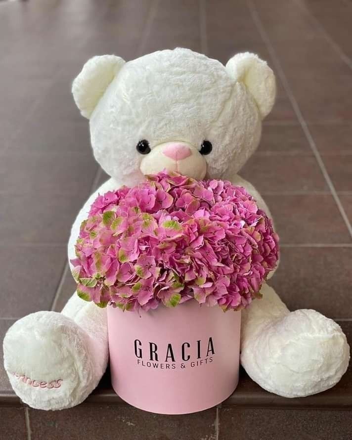 a white teddy bear holding a bouquet of pink hydrangeas in a pink vase