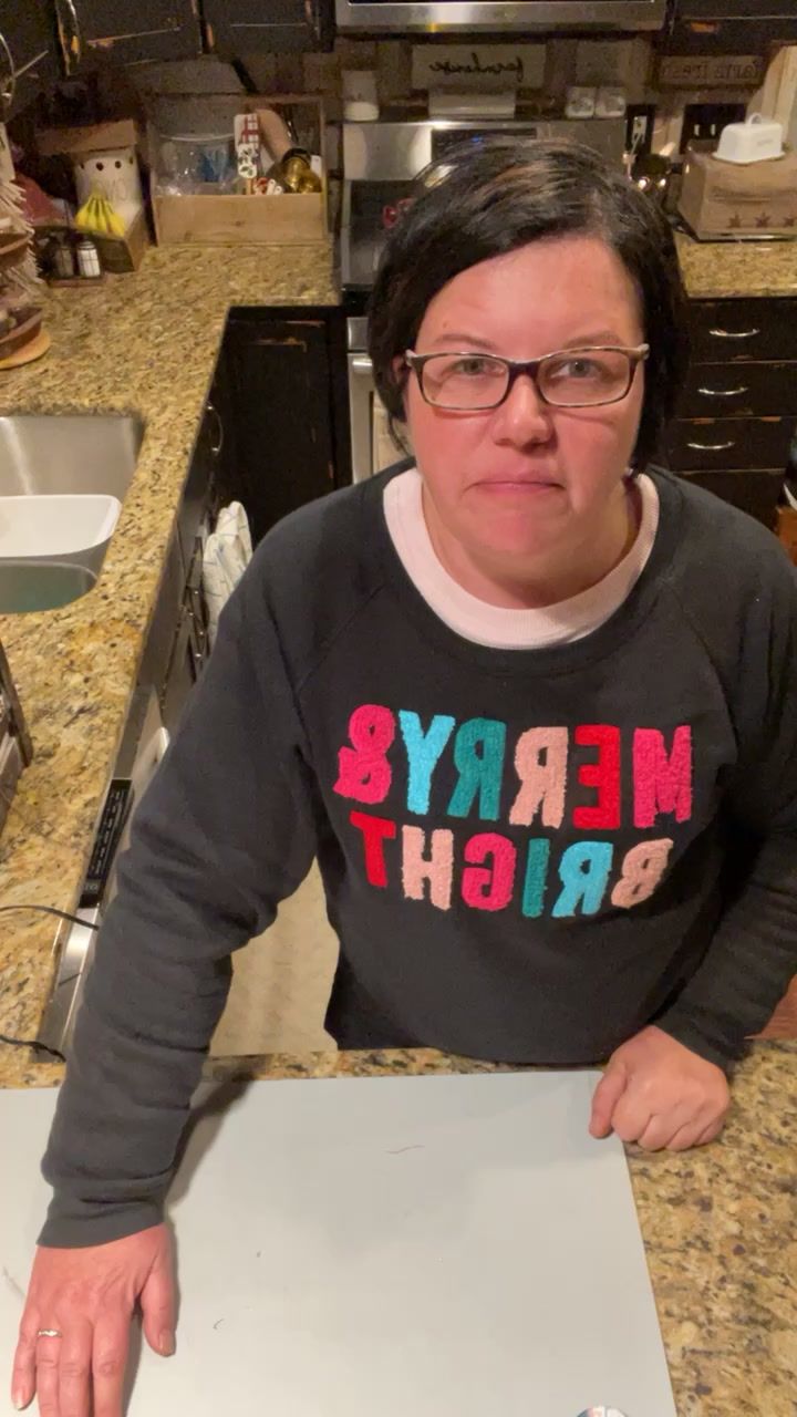 a woman sitting at a kitchen counter with a cake in front of her and the words merry & bright on it