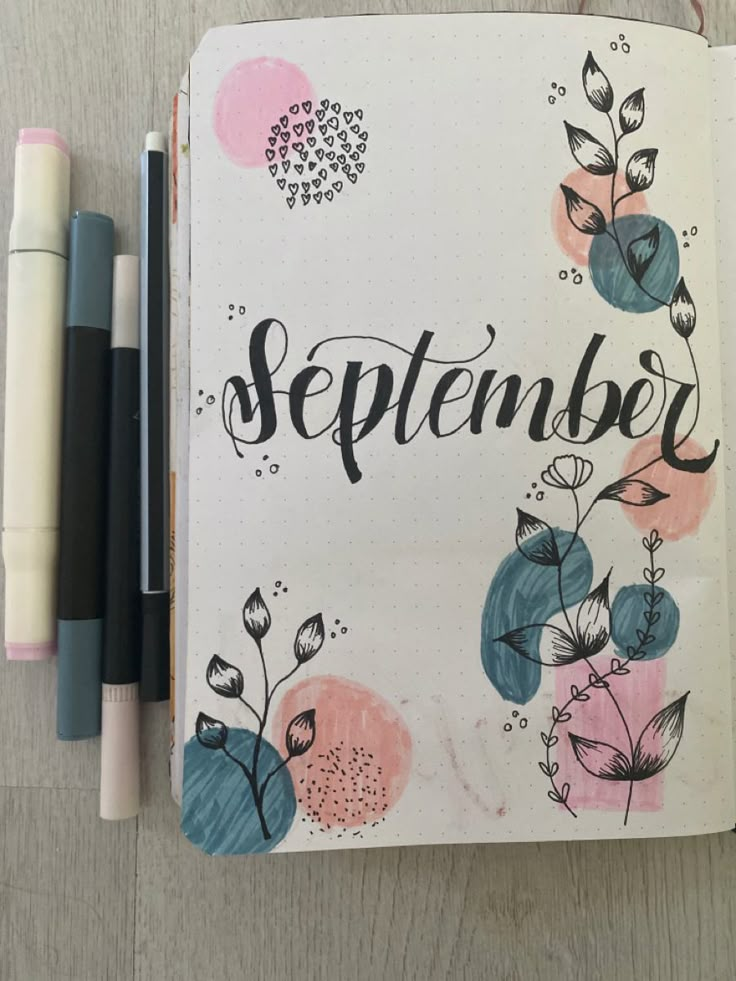 an open notebook with the word september written in cursive writing on it next to two markers