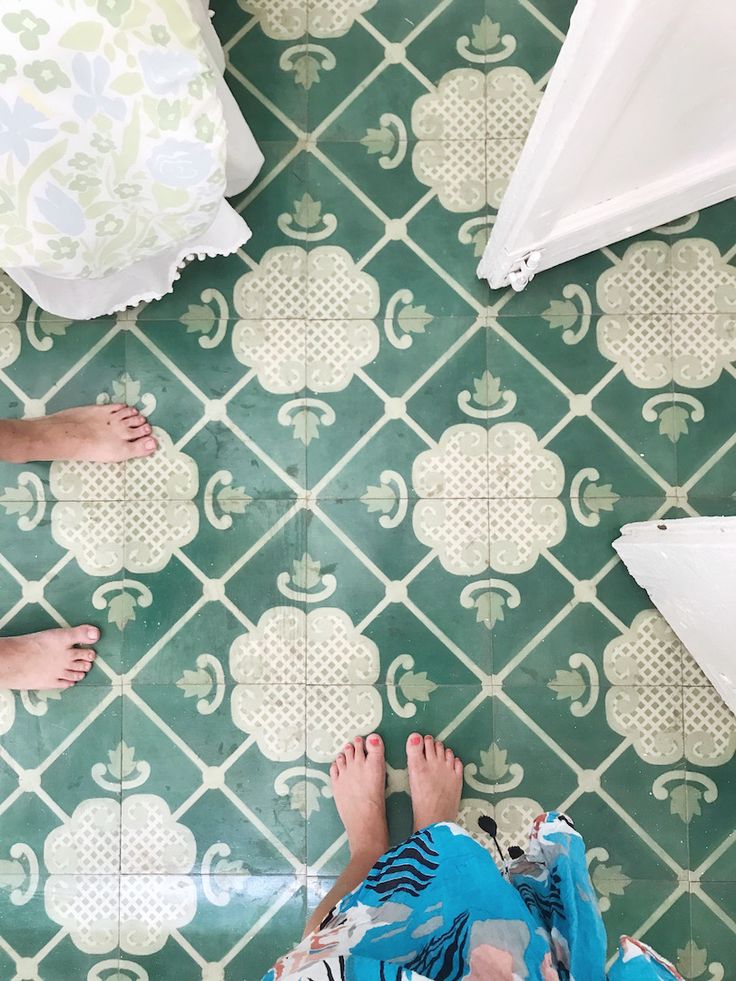 two people standing in front of a green and white tile floor with flowers on it